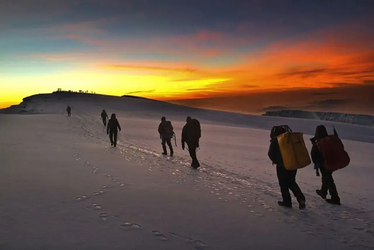 Randonneurs escaladant le Kilimandjaro au lever du soleil, vue sommet. Le ciel embrasé offre un spectacle inoubliable.