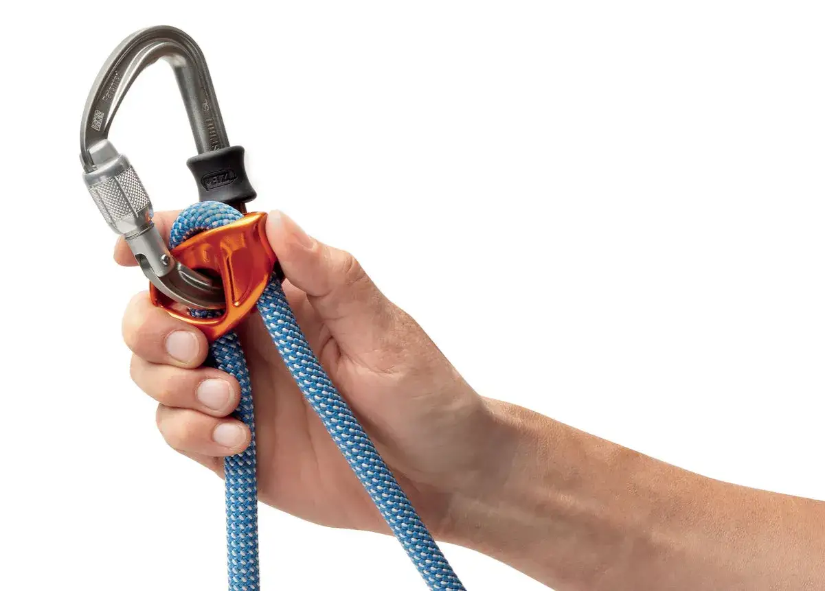 Main tenant une cordelette bleue et blanche avec un mousqueton et un assureur Petzl. La longe dynamique est prête pour l'escalade.