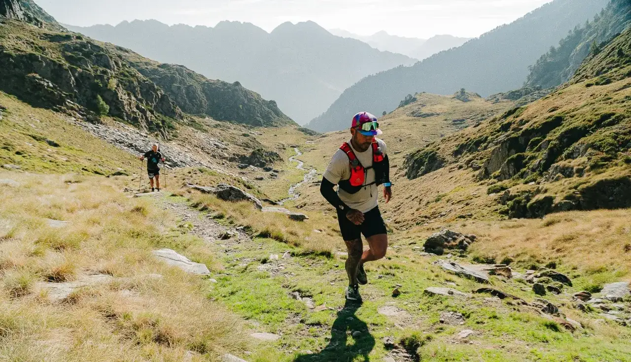 Deux coureurs s'attaquent au transpyrénéenne trail dans un paysage montagneux spectaculaire, entre herbes sèches et rochers.