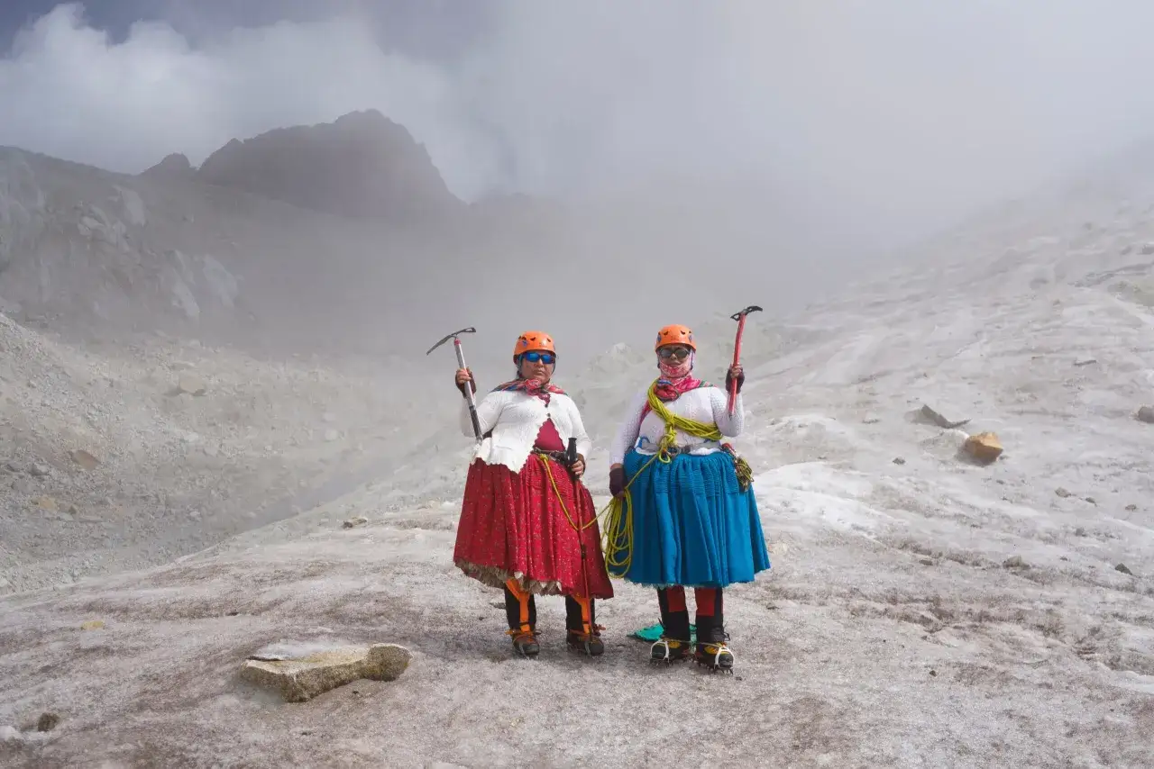 Deux cholitas escaladoras, fi&egrave;res et &eacute;quip&eacute;es de piolets, posent sur un glacier brumeux.