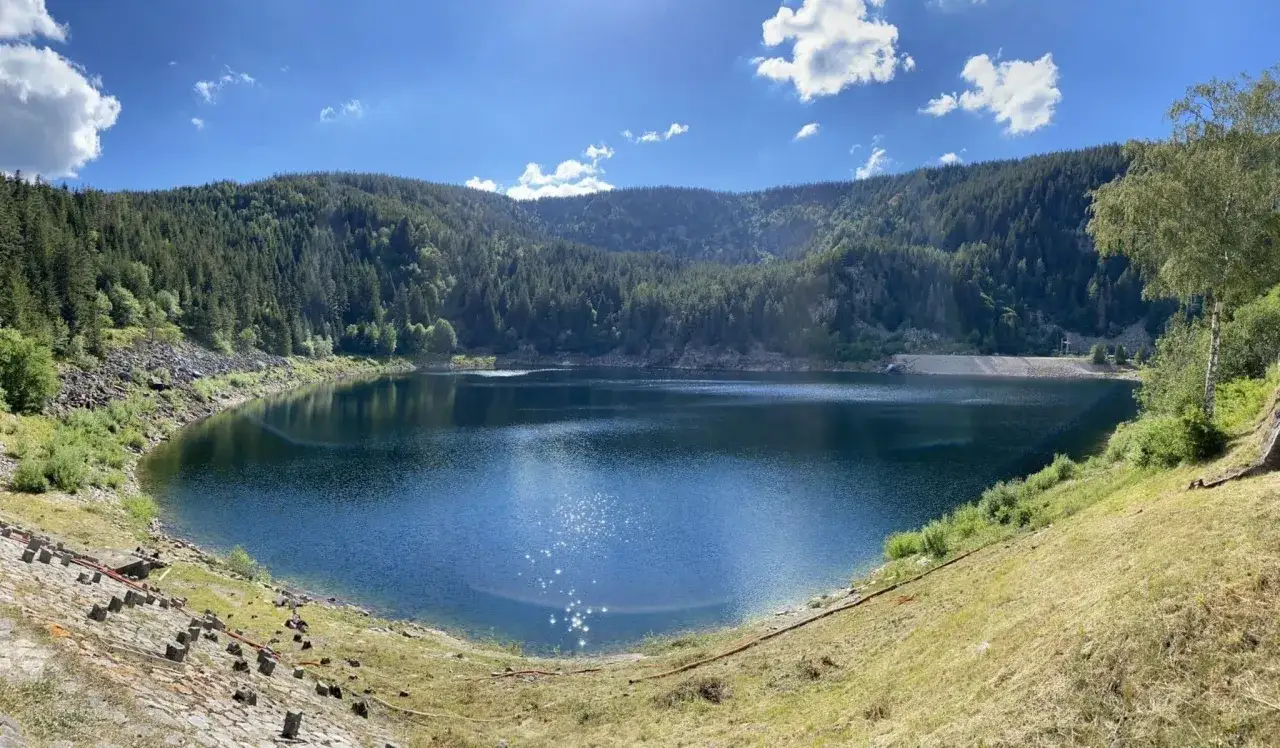 Lac bleu entour&eacute; de for&ecirc;ts verdoyantes, parfait pour une balade Vosges facile. Le soleil scintille sur l'eau calme.