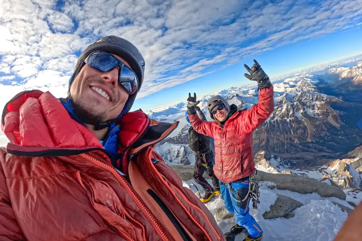 Lise Billon et ses compagnons célèbrent au sommet, entourés de montagnes enneigées sous un ciel bleu éclatant.