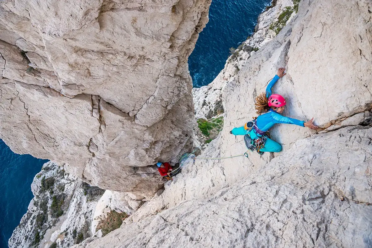 Grimpeurs dans les Calanques, un guide escalade calanques parfait pour l'aventure. L'eau bleue en contrebas contraste avec la roche claire.