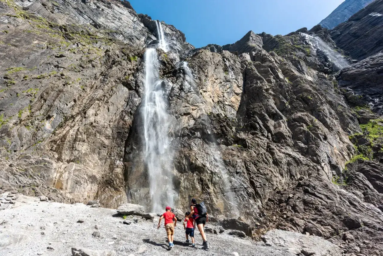 Famille en randonn&eacute;e sur la ruta circo de Gavarnie, admirant la cascade spectaculaire tombant d'une falaise rocheuse.