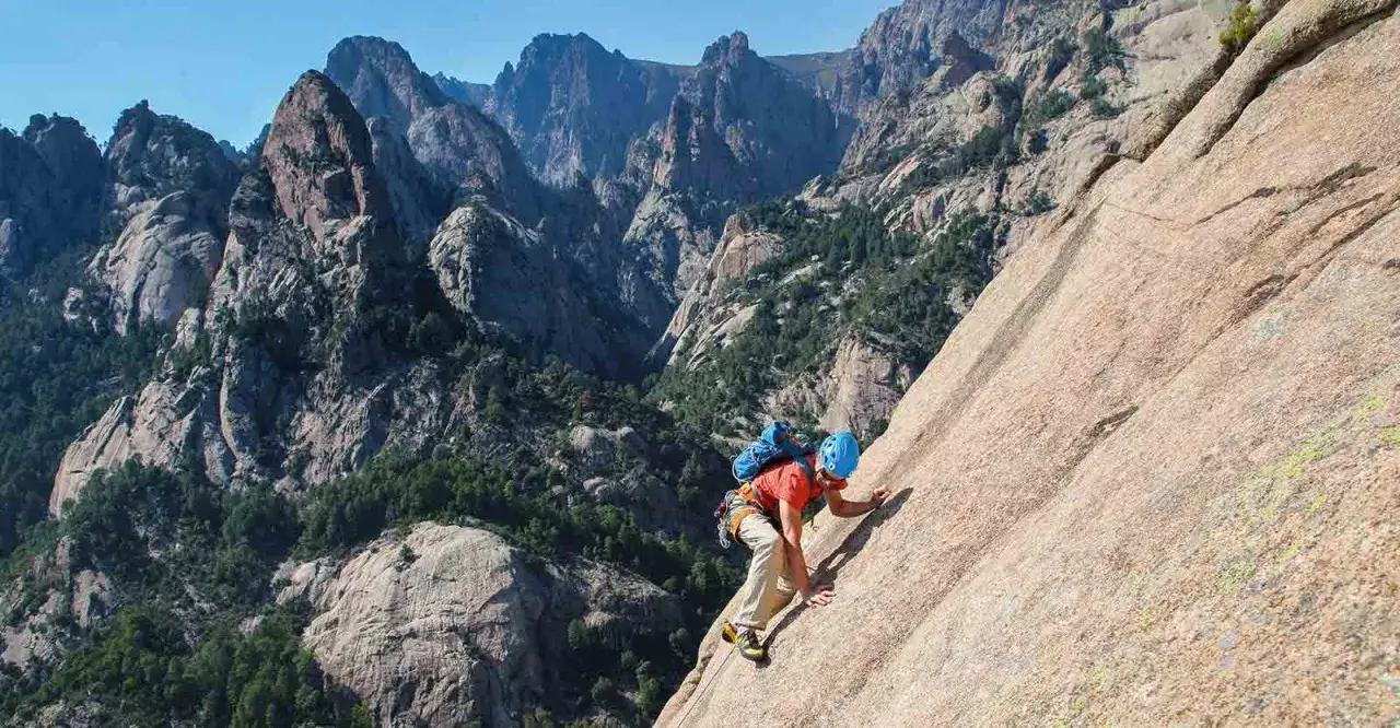 Un grimpeur en plein effort sur un rocher, avec les majestueuses montagnes de Bavella en arrière-plan. L'escalade bavella offre des vues spectaculaires.