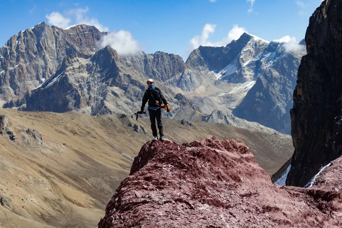 J&eacute;r&eacute;my Big&eacute;, un alpiniste, se tient au sommet d'une cr&ecirc;te rocheuse rouge, dominant un paysage montagneux spectaculaire sous un ciel bleu.