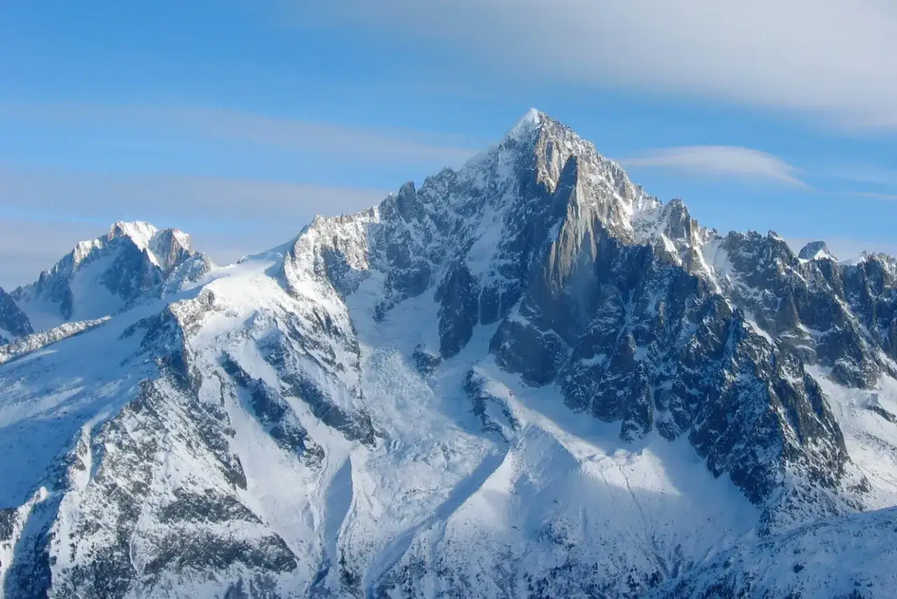 Le majestueux Aiguille Verte se dresse, couvert de neige, sous un ciel bleu clair.