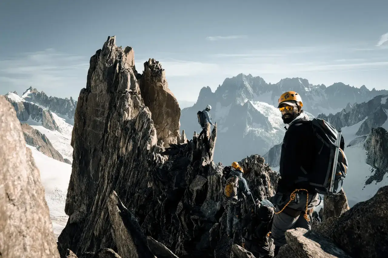 Antoine Cayrol et son &eacute;quipe escaladent un pic rocheux escarp&eacute;, avec des montagnes enneig&eacute;es en arri&egrave;re-plan.