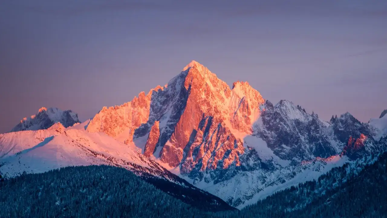 Le soleil embrase le sommet d'une montagne enneigée, projetant des ombres profondes sur les pentes. Un spectacle grandiose.