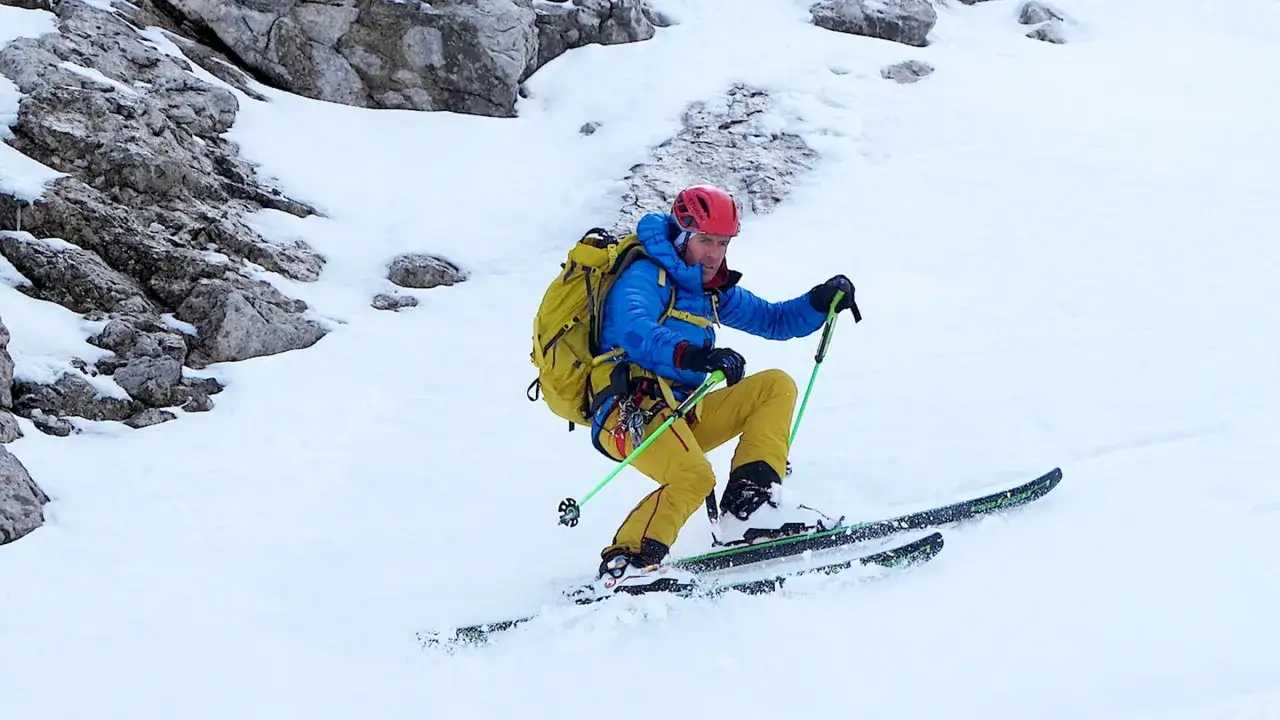 Davo Karnicar, skieur alpin, descend une pente enneigée, bâtons de ski en main, casque rouge et sac à dos jaune.