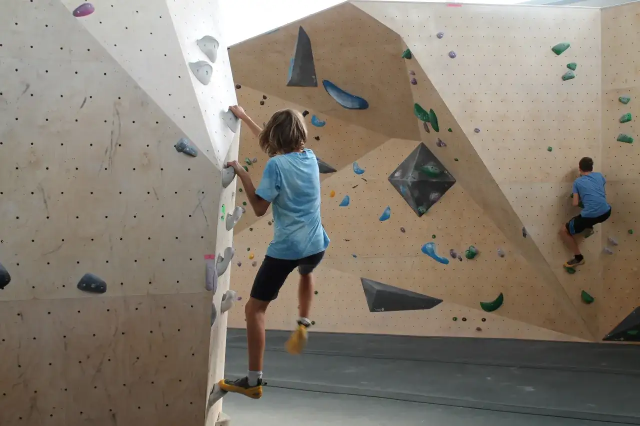 Deux jeunes grimpeurs s'entraînent sur un mur d'escalade, atteignant le hueco zenith de leurs voies.