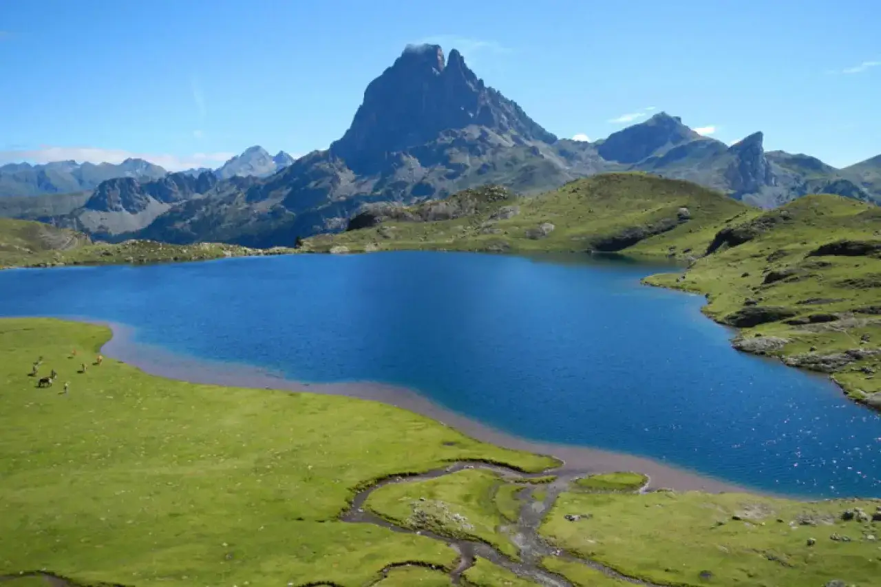 Lac bleu &eacute;tincelant au parque nacional de los Pirineos, entour&eacute; de montagnes verdoyantes et d'un pic imposant. Quelques chevaux paissent paisiblement sur la rive.