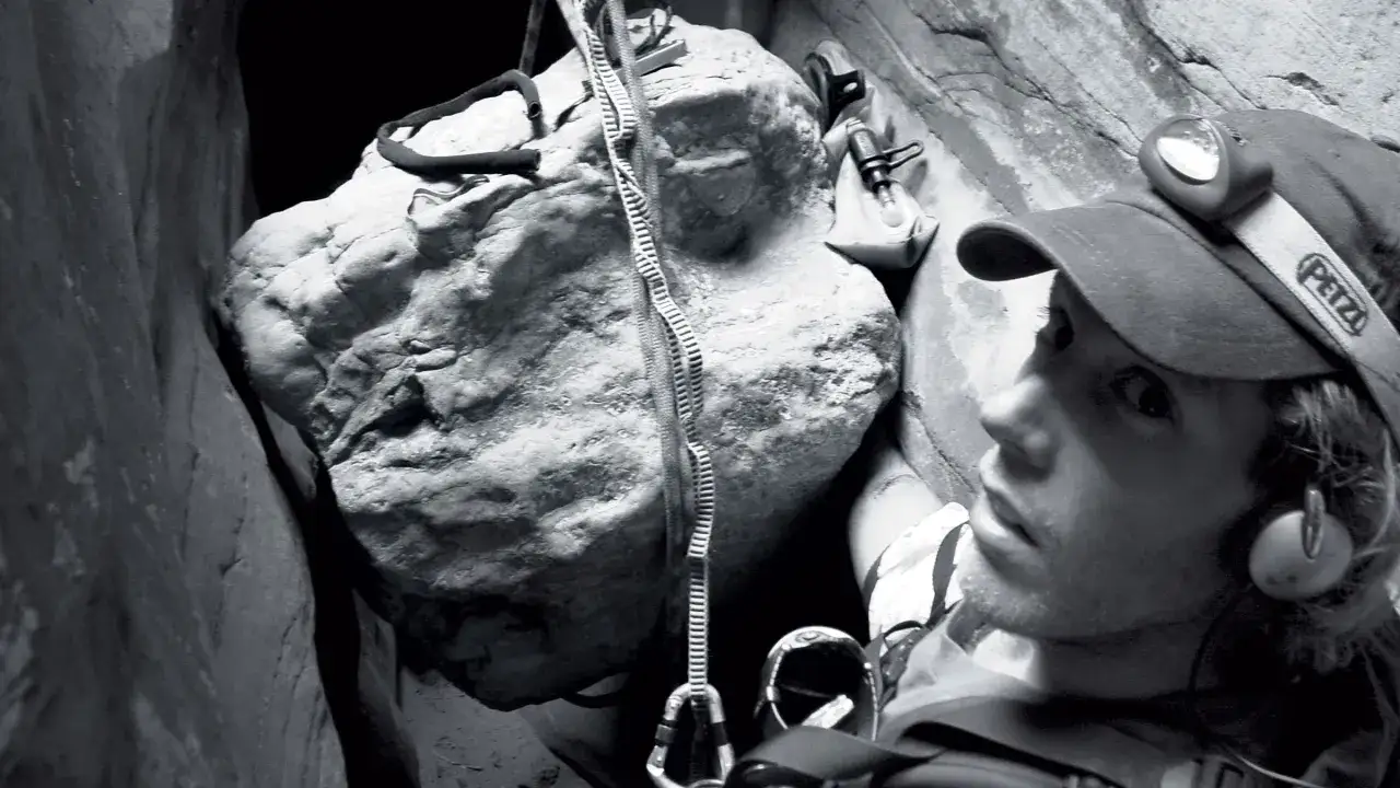 Aron Ralston, le visage marqu&eacute;, est coinc&eacute; dans un canyon, une corde &agrave; la main, face &agrave; un rocher mena&ccedil;ant.
