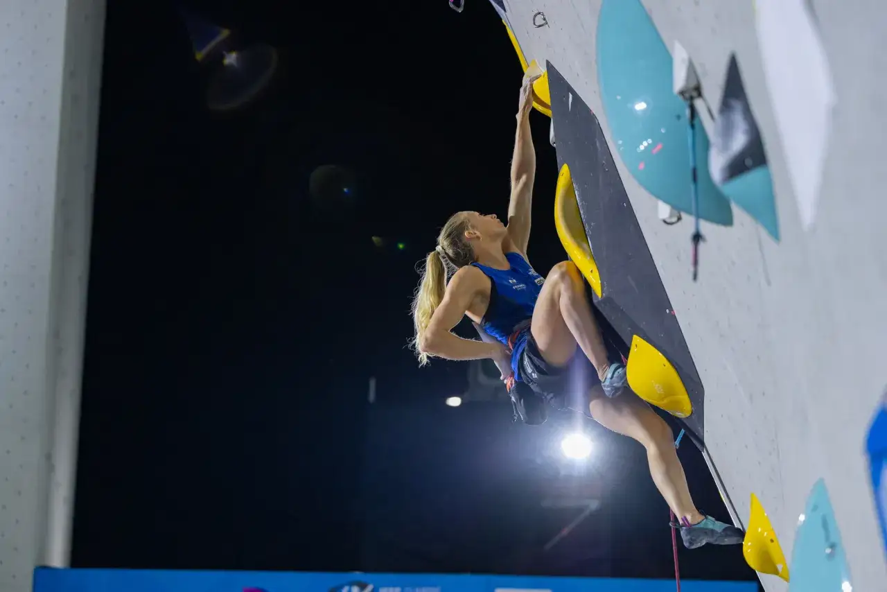 Manon Hilly, grimpeuse française, s'élève sur un mur d'escalade, ses muscles tendus dans un effort concentré.