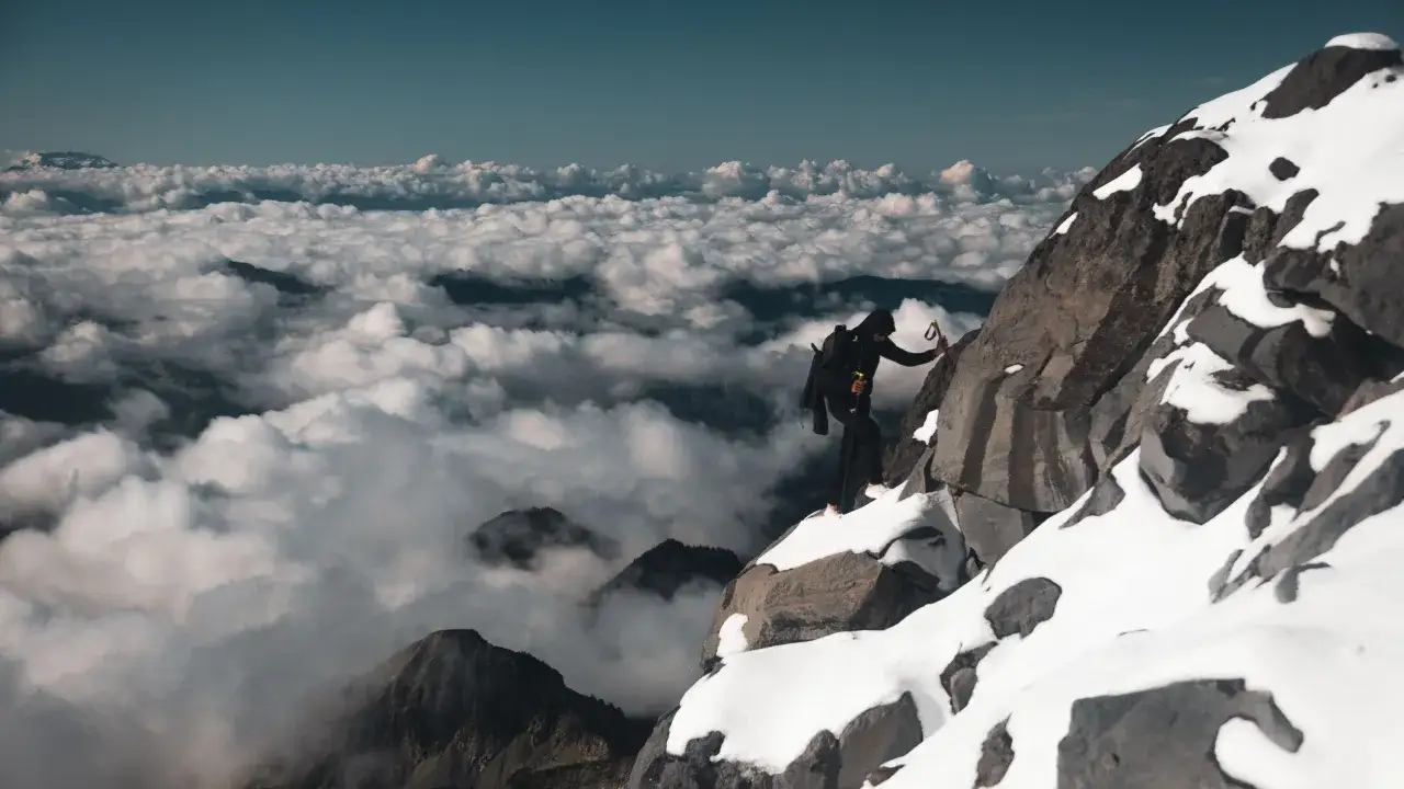 Un alpiniste escalade un sommet enneigé, au-dessus d'une mer de nuages. Un aperçu du film Kilian Jornet.