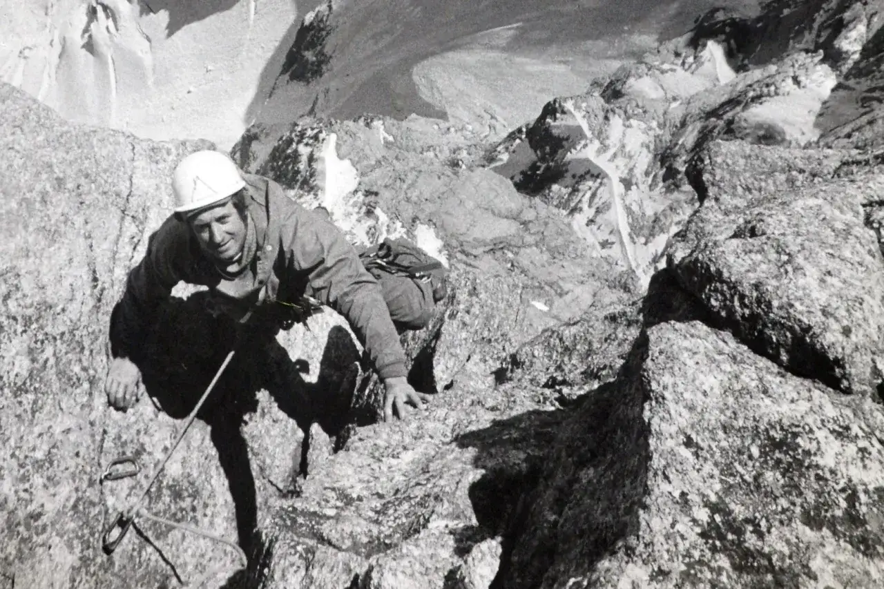 Serge Gousseault, casque blanc, escalade une paroi rocheuse escarp&eacute;e, le regard d&eacute;termin&eacute;.