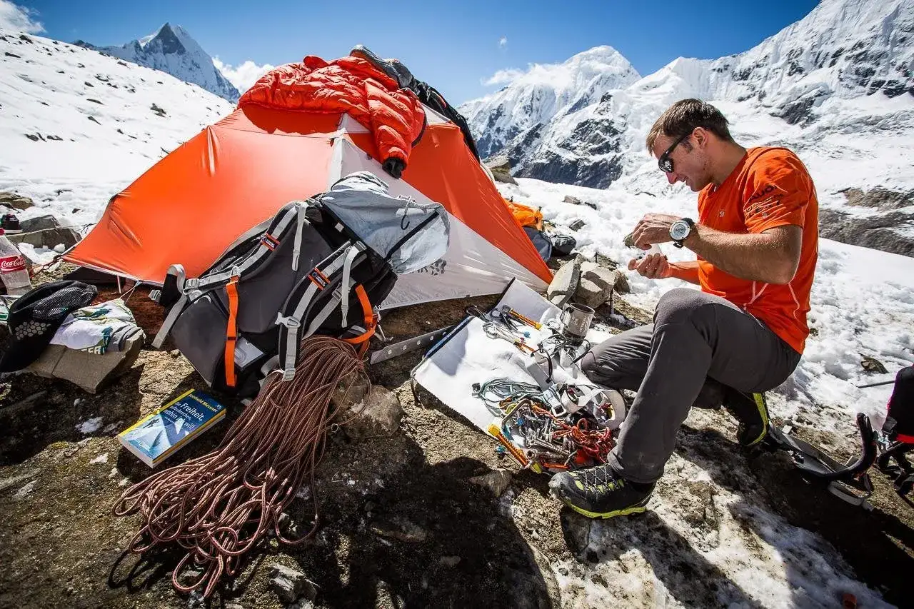 Ueli Steck, mort, prépare son matériel d'escalade près de sa tente orange, au milieu des montagnes enneigées.