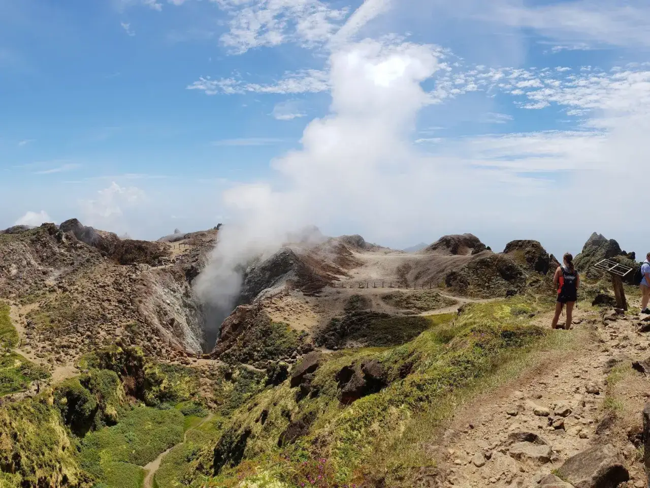 Vue panoramique d'une montagne en Guadeloupe, avec un crat&egrave;re fumant et des randonneurs admirant le paysage volcanique.