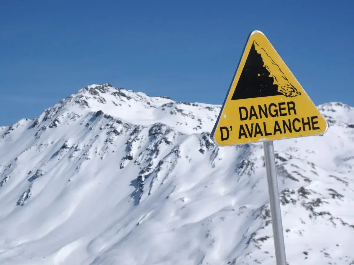 Panneau jaune triangulaire signalant le danger d'avalanche sur fond de montagnes enneig&eacute;es et de ciel bleu. Les neiges mouvantes invitent &agrave; la prudence.