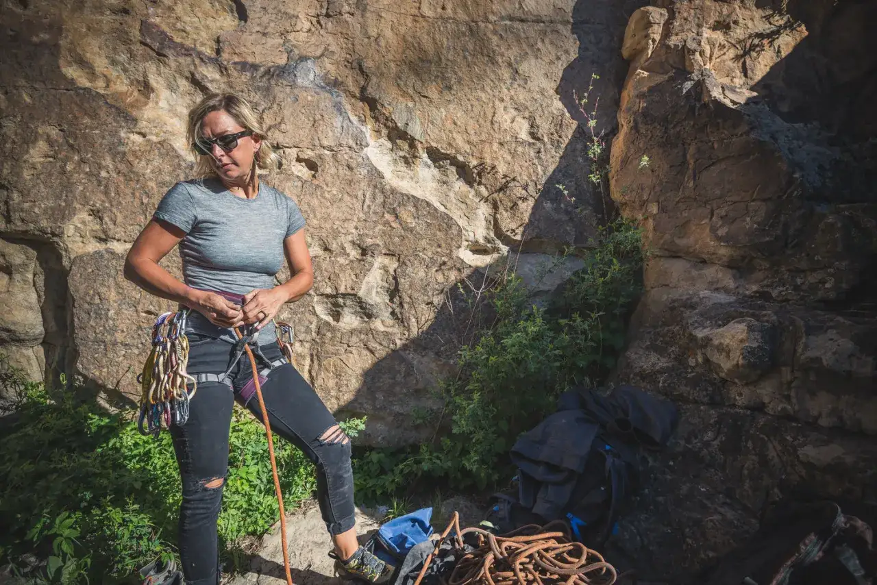 Femme préparant sa tenue d'escalade, harnais et dégaines prêts pour l'ascension.