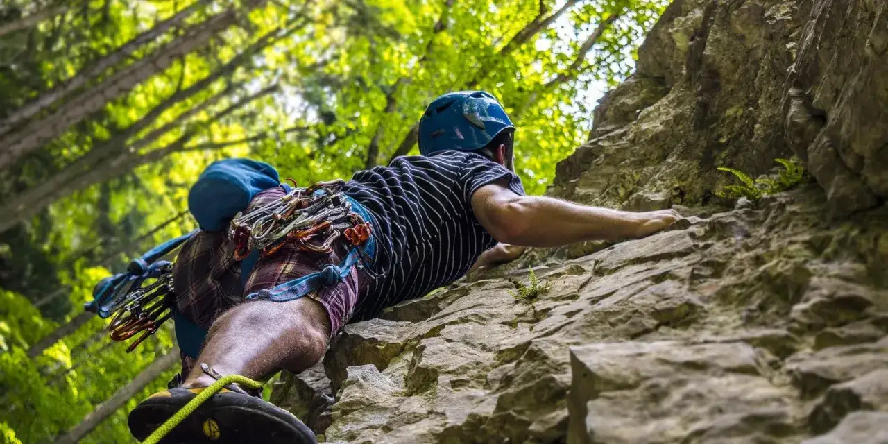 Un grimpeur équipé pour l'escalade en Ariège progresse sur une paroi rocheuse, entouré par la verdure.