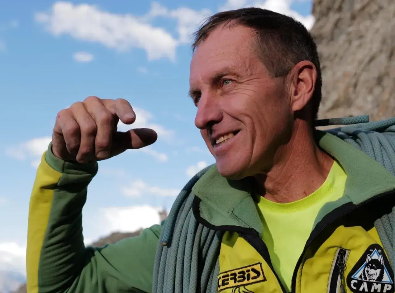 Denis Urubko, alpiniste exp&eacute;riment&eacute;, sourit sous un ciel bleu, une corde d'escalade autour du cou.