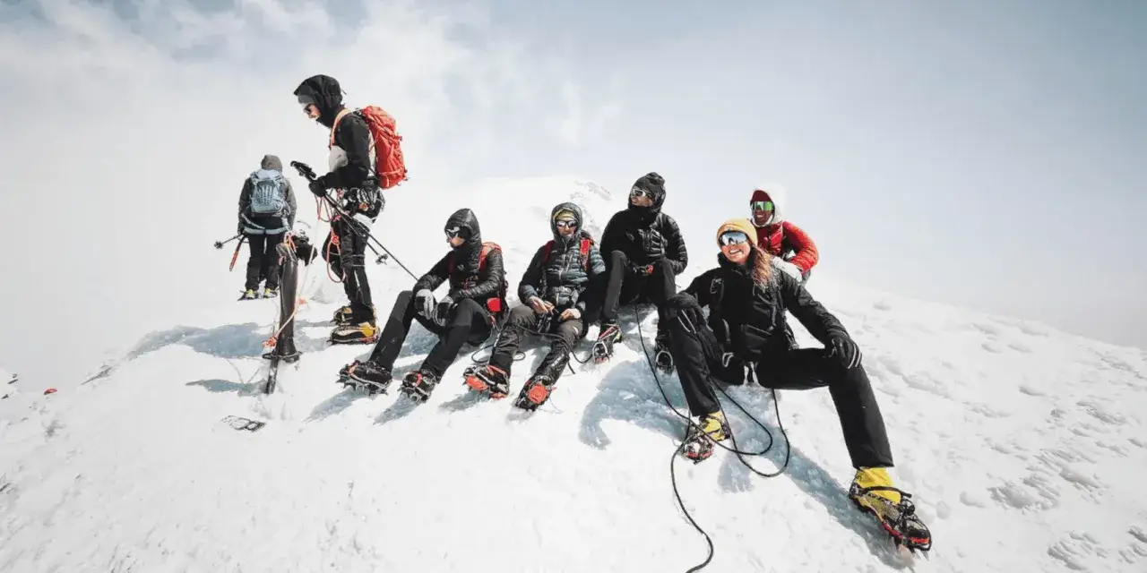 Une &eacute;quipe de grimpeurs, dont Balin Miller, se repose sur une cr&ecirc;te enneig&eacute;e, &eacute;quip&eacute;s de crampons et de piolets, pr&ecirc;ts pour l'ascension.