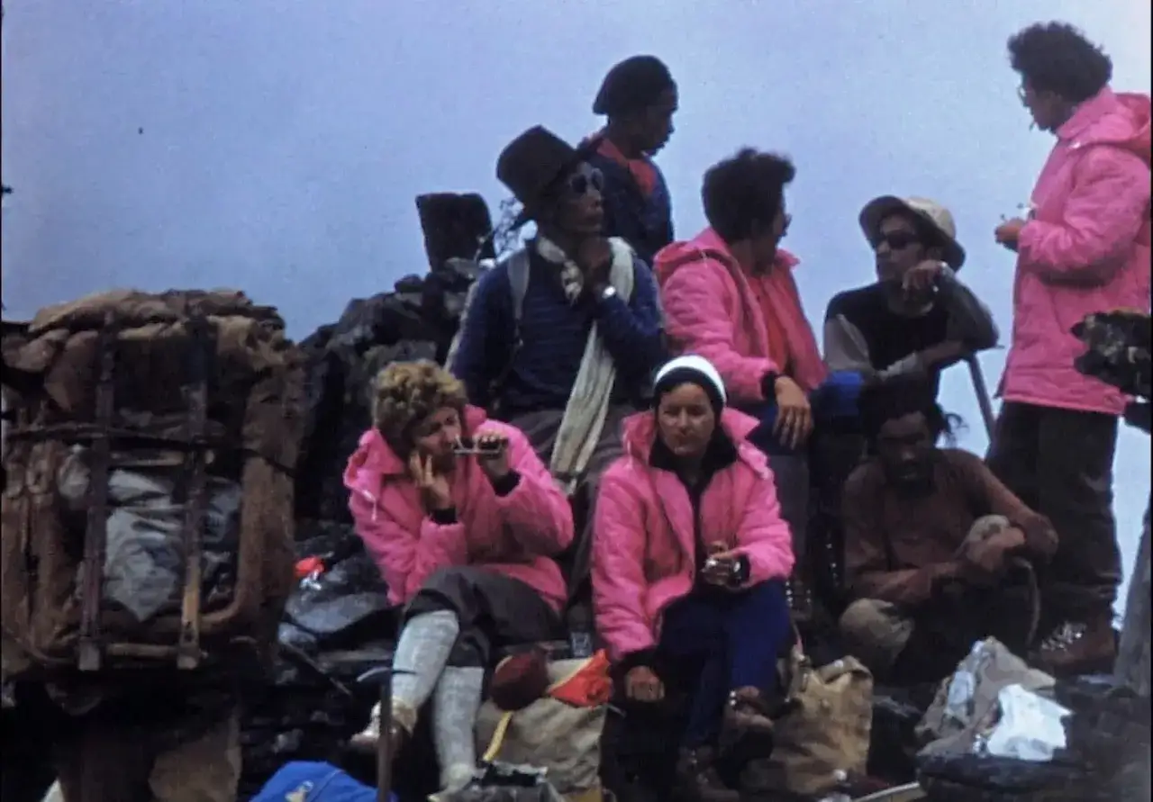 Groupe de randonneurs, dont Claude Kogan, se reposant sur un flanc de montagne, v&ecirc;tus de vestes roses vives.